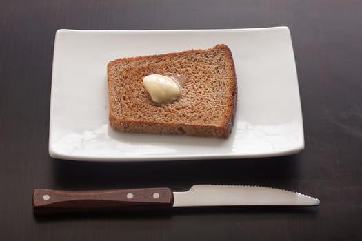 Top view of toasted rye bread with butter on the white plate