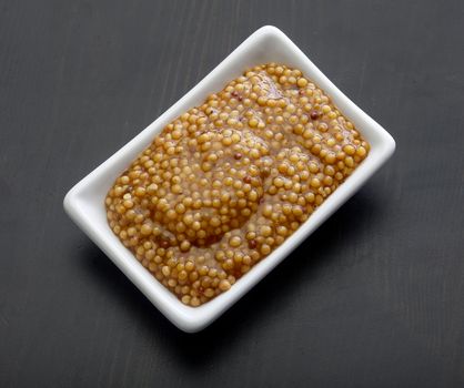 Top view of white plate with grainy mustard on the black wooden table