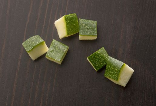 Top view of cubes of green zucchini on the black wooden table