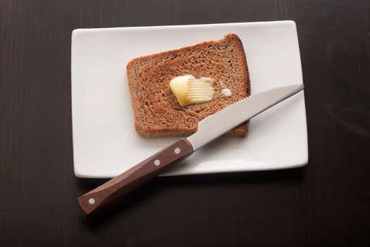 Top view of toasted rye bread with butter on the white plate