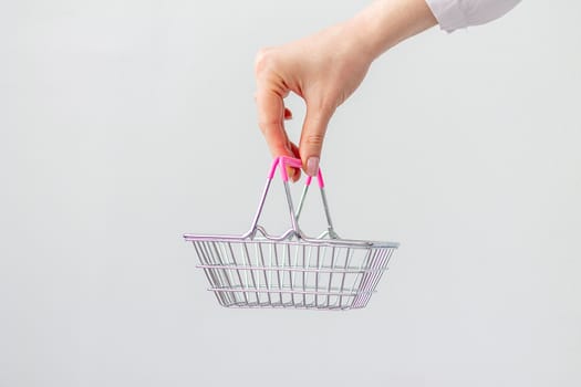Close-up of a woman's hand horizontally holding a toy small metal shopping basket with a pink plastic handle isolated on a white background. The concept of shopping. copy space for advertising