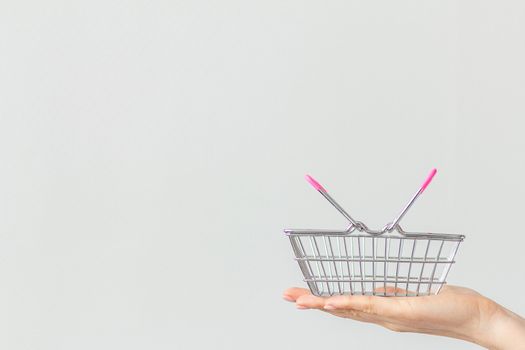 Close-up of a woman's hand holding in the palm of her hand a small metal shopping basket with a pink plastic handle isolated on a white background. copy space for advertising. concept of shopping.