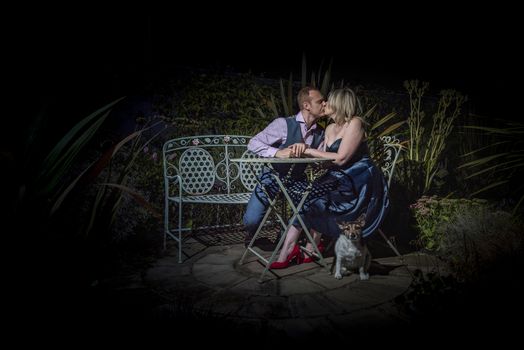 Quorn, UK - Aug 2019: Couple kissing on a garden bench at night, dog in forground