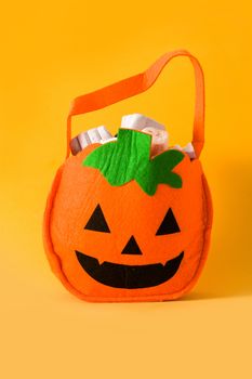 Hand holding Halloween pumpkin bag with candies inside isolated on yellow background