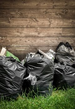 Three full black plastic bag in park in the background of wooden wall.