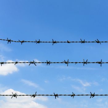 Barbed wire against blue sky and clouds