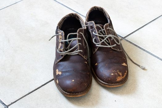 Scuffed and old leather shoes/boots on a tiled floor