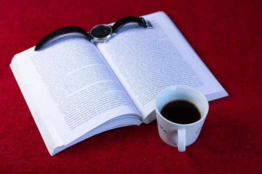 Coffee, with an open book and a black watch on a red sofa/couch