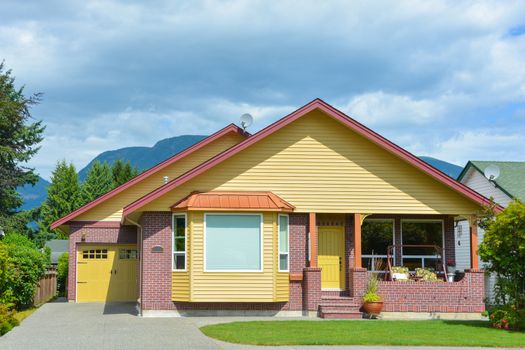 Yellow residential house with accurate lawn in front and concrete driveway to the garage