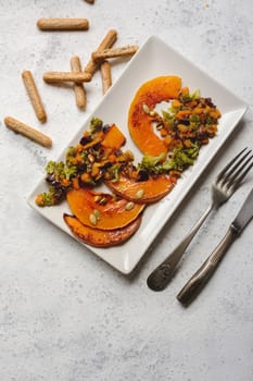sliced baked pumpkin, with broccoli and assorted vegetables, on rectangular white plate, from above
