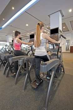 Two young women on step machines at a gym