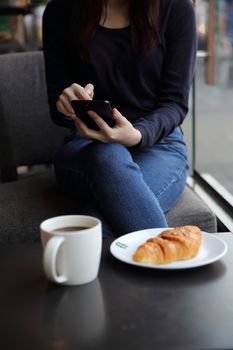 Asian female typing text message with coffe and Croissant