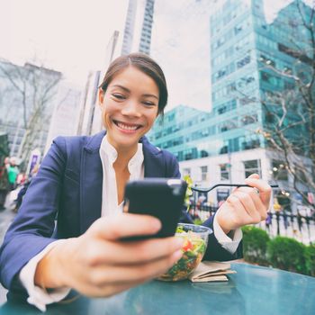 Young business woman on smartphone eating salad on lunch break in City Park living healthy lifestyle working on smart phone. Happy multiracial businesswoman, Bryant Park, manhattan, New York City, USA