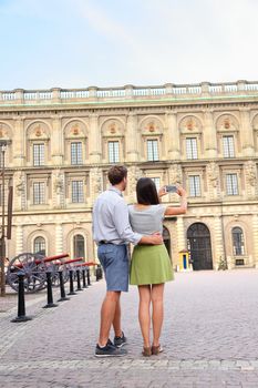 Tourists couple taking photo of picture with smartphone of Stockholm Royal Palace, Sweden, Europe. Happy tourist people in visiting landmark attractions in Gamla Stan, the old town of Stockholm.