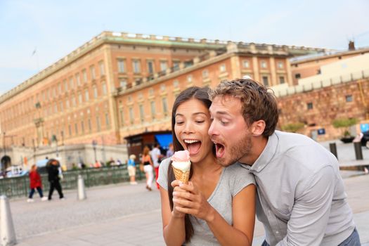 Couple eating ice cream having fun making funny expression together in Stockholm, Sweden, Europe. Happy multiracial young couple by the Royal Palace. Scandinavian man, Asian woman.