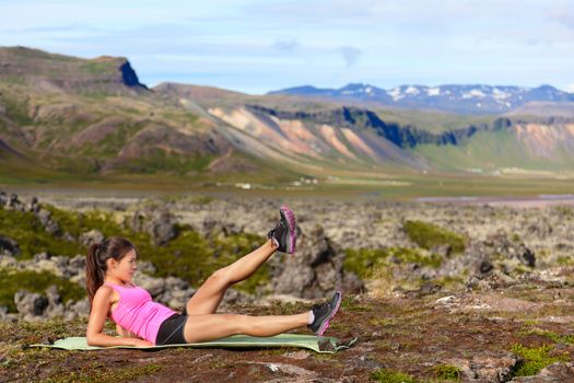 Fitness woman exercising in nature working on core strength doing scissor kick and flutter kicks exercise outdoor in amazing landscape on Iceland.