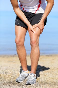 Muscle injury. Man runner with sprain thigh muscles. Athlete running in sports shorts clutching his thigh muscles after pulling or straining them while jogging on the beach.