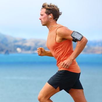 Running app on smartphone. Male runner listening to music jogging with armband for smart phone. Fit man fitness model working outdoor by water.