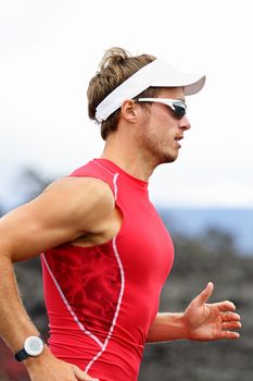 Running triathlon athlete man. Runner triathlete training for ironman wearing sports sunglasses. Young Male athlete running in red compression top.