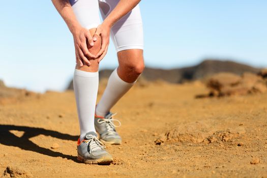 Running injury - Male runner with knee pain. Trail runner injured jogging in nature clutching his knee in pain. Man fitness athlete.