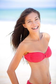 Bikini beach asian caucasian woman smiling happy on travel vacation holidays by blue ocean sea at tropical resort. Cheerful smiling excited mixed race girl laughing full of joy looking at camera.
