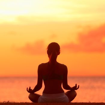 Meditation - Meditating yoga woman at at serene beach sunset. Girl relaxing in lotus pose in calm zen moment in the ocean water during yoga holidays resort retreat. Multiracial girl.