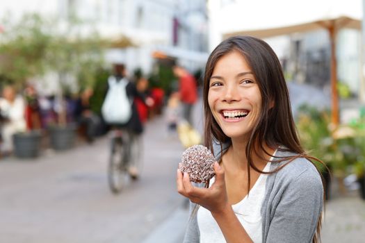 Woman eating traditional danish food floedeboller also called cream buns or marshmallow teacake. Girl enjoying the chocolate covered treat outside in city street of Copenhagen, Denmark.