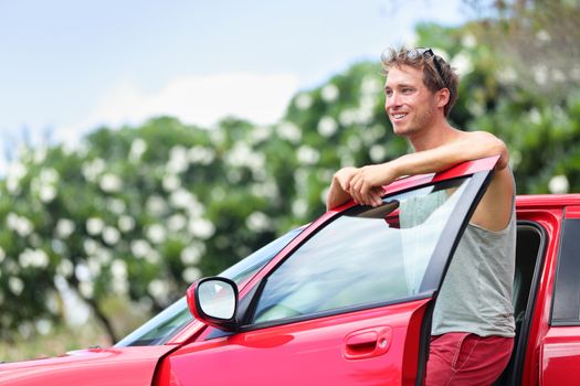 Car owner - young man and new red car outside. Happy male model leaning on door of a red sports car smiling.
