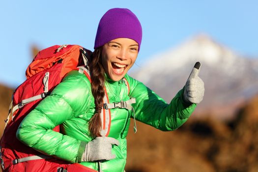 Hiking woman in winter jacket giving thumbs up smiling. Young Asian woman hiker smiling joyful at camera outdoor on hike trip. Beautiful young mixed race Asian Chinese / Caucasian woman in mountain.