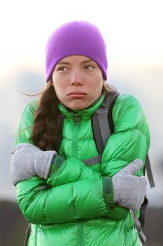 Freezing woman feeling cold outdoors trying to keep warm shaking and shivering wearing hat and gloves outside hiking on hike.