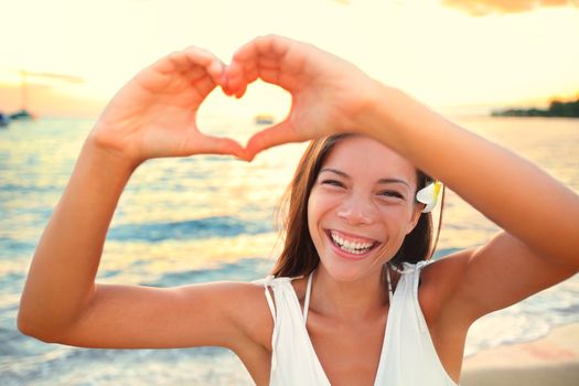 Love vacation - woman showing heart on beach. Girl gesturing heart shaped hands smiling happy and loving at camera. Pretty joyful multicultural Asian Caucasian girl.