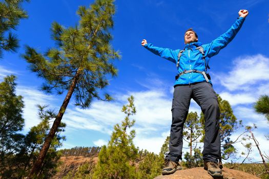 Man hiking reaching summit top cheering celebrating on mountain top with arms up outstretched towards the sky. Happy male hiker.