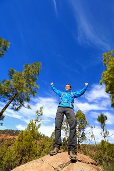 Hiking man reaching summit top cheering celebrating on mountain top with arms up outstretched towards the sky. Happy male hiker.