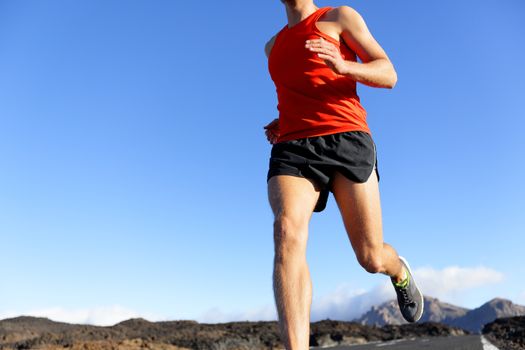 Runner man closeup - male athlete running on road sprinting. Unrecognizable person under blue sky.