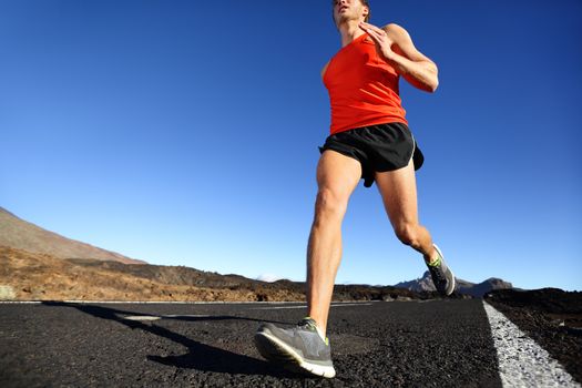 Sprinting running man - male runner training outdoors jogging on mountain road in amazing landscape nature. Close up of fit handsome jogger working out for marathon outside in summer.