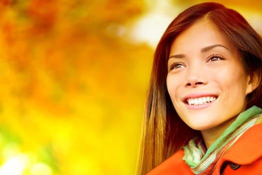 Autumn / Fall woman in colorful foliage in city park forest smiling happy. Portrait of modern girl and colorful leaves outdoor in fall forest foliage. Mixed race Asian Caucasian female model.