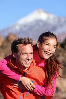 Happy couple piggyback in active lifestyle having fun on hike. Fresh young joyful interracial couple. Asian woman hiker and Caucasian man in outdoor activity on Teide, Tenerife, Canary Islands, Spain