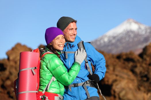 Campers couple hiking enjoying looking at view embracing in love. Romantic hiker man and woman wearing backpacks enjoying sunset during hike on mountain volcano Teide, Tenerife, Canary Islands, Spain.