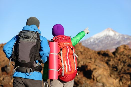 Hikers looking at view pointing hiking in mountain. People hiker couple in nature landscape trekking wearing backpacks. Woman and man on volcano Teide, Tenerife, Canary Islands, Spain