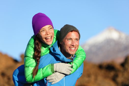 Couple piggyback happy in active lifestyle having fun on hike. Fresh young joyful interracial couple. Asian woman hiker and Caucasian man in outdoor activity on Teide, Tenerife, Canary Islands, Spain