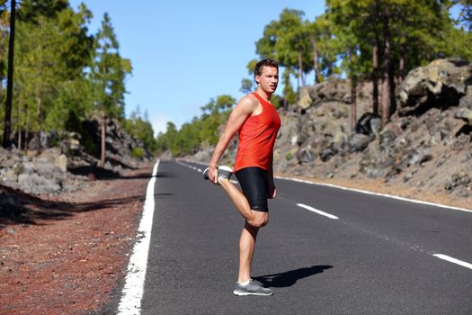 Runner man stretching thigh and legs after running on mountain forest road in. Handsome Caucasian male fitness model outdoors.