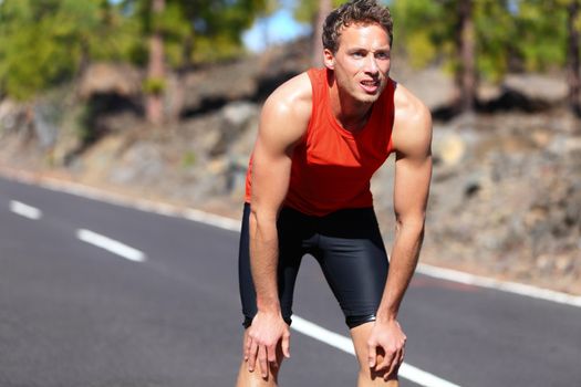 Runner resting after running. Jogging man taking a break during training outdoors in on mountain road. Young Caucasian male fitness model after work out.