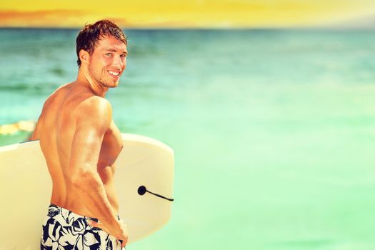 Surfer man going surfing on summer beach. Male bodyboarding surfing man good looking standing with bodyboard surfboard during vacation holidays getaway. Caucasian water sport model in his 20s.