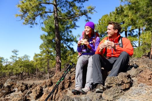 Couple eating lunch taking a break hiking enjoying sandwiches. Hikers living active lifestyle in mountain nature. Woman and man hiker sitting on hike on volcano Teide, Tenerife, Canary Islands, Spain.