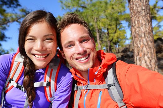 Selfie couple taking self-portrait hiking using smart phone camera in nature. Happy couple taking self-portrait photo picture looking at camera smiling happy. Man and woman having fun together.