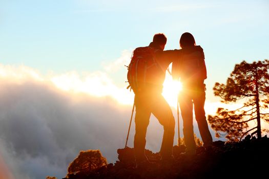 Hiking adventure healthy outdoors people standing talking. Couple enjoying sunset view above the clouds on trek. Video of young woman and man in nature wearing hiking backpacks and sticks.