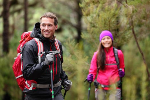 Hiking man and woman on hike in forest trekking. Couple on adventure trek in beautiful forest nature. Multicultural Asian woman and Caucasian man living healthy active lifestyle in woods.