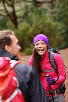 Couple having fun laughing hiking in forest. Multicultural woman and man hikers on hike in woods wearing backpacks outdoors in nature.