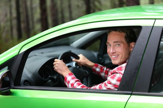 Electric car driver - green energy biofuel concept. Male behind wheel. Man driving new vehicle in cheerful in nature forest. Young male driver looking at camera with arm raised cheering.