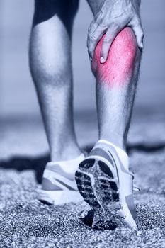 Muscle injury - Man running clutching calf muscle after spraining it while out jogging on the beach. Male athlete sport injury.